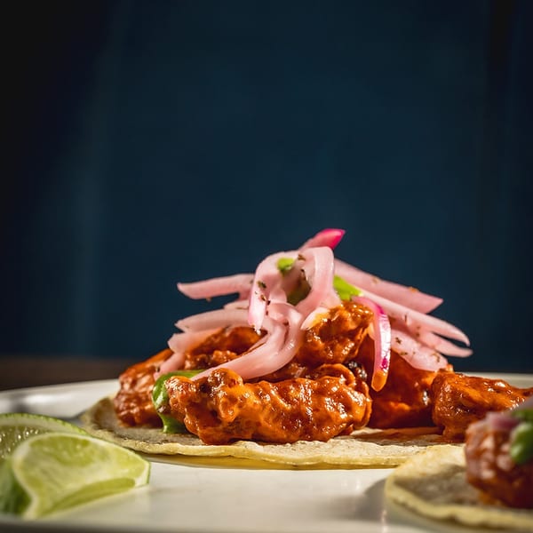 Close-up of a vibrant chicken taco topped with pickled red onions and lime wedges.