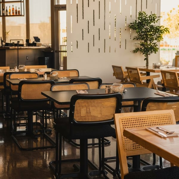 Modern restaurant interior with black tables, cane-backed chairs, and a decorative white wall.