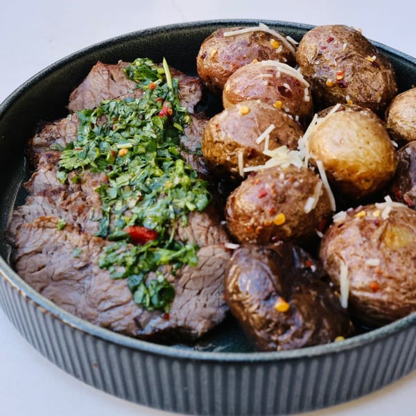Steak with green chimichurri sauce and roasted baby potatoes topped with cheese and chili flakes.