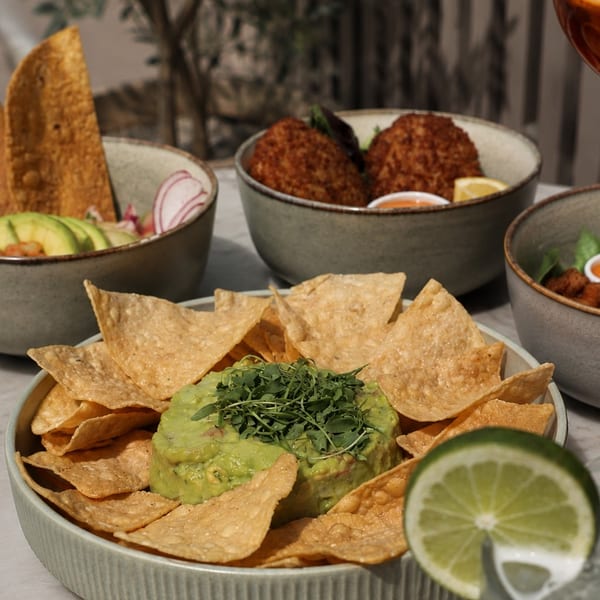 Guacamole with tortilla chips, ceviche, and fried croquettes on a marble table.