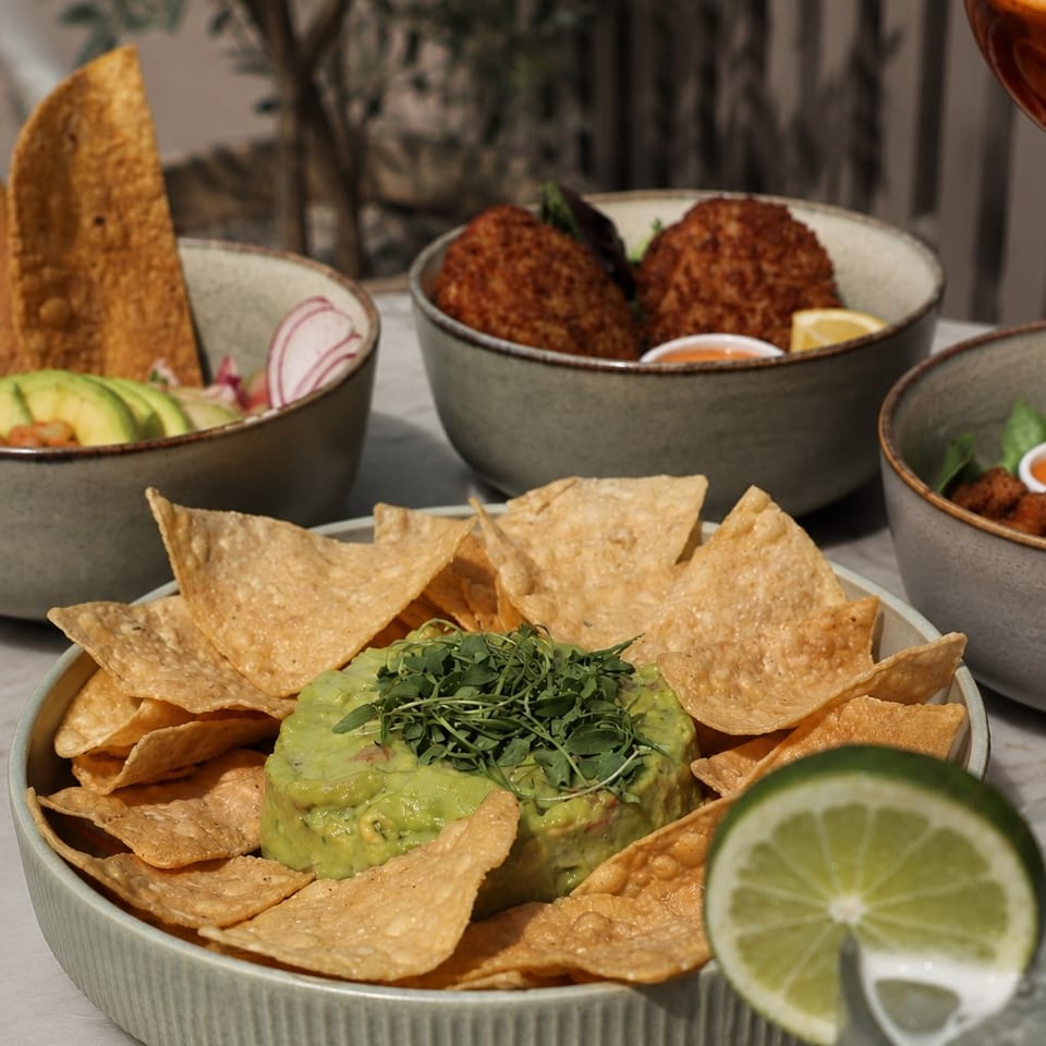 Guacamole with tortilla chips, ceviche, and fried croquettes on a marble table.