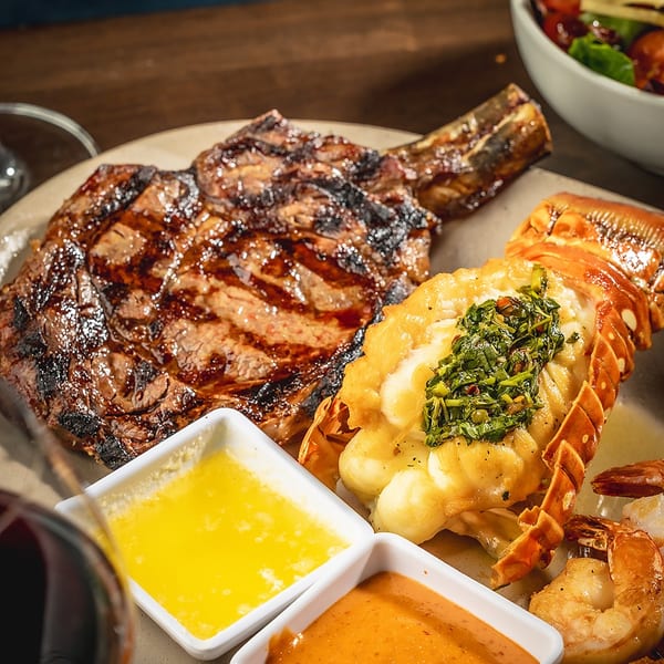 Grilled steak and lobster tail with sauces, shrimp, and a side salad.