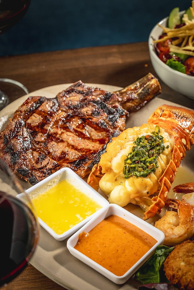 Grilled steak and lobster tail with sauces, shrimp, and a side salad.