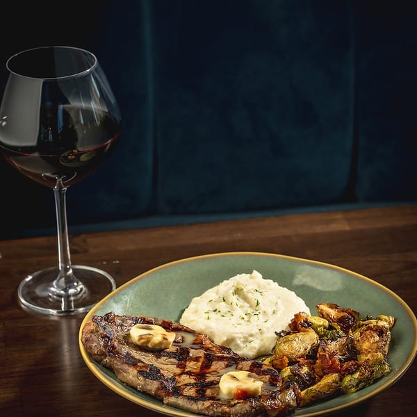 Grilled steak with mashed potatoes and roasted vegetables, next to a glass of red wine.