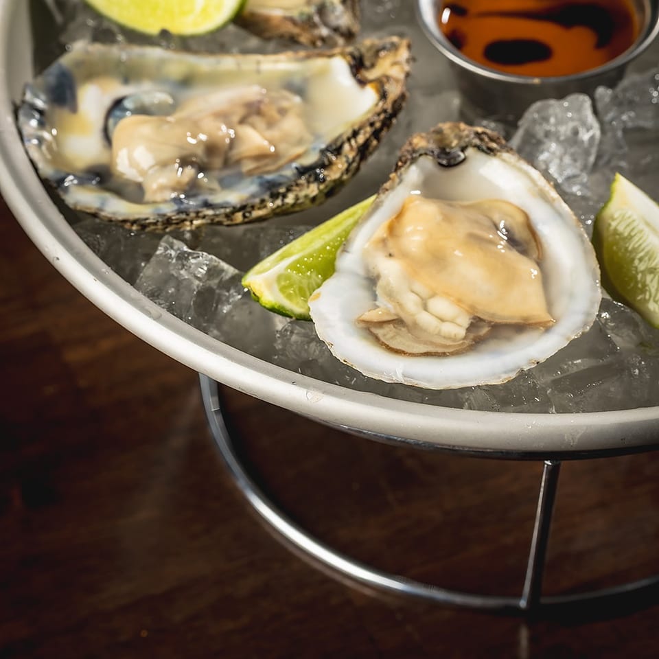 Fresh oysters on ice with lime wedges and a small bowl of dipping sauce.
