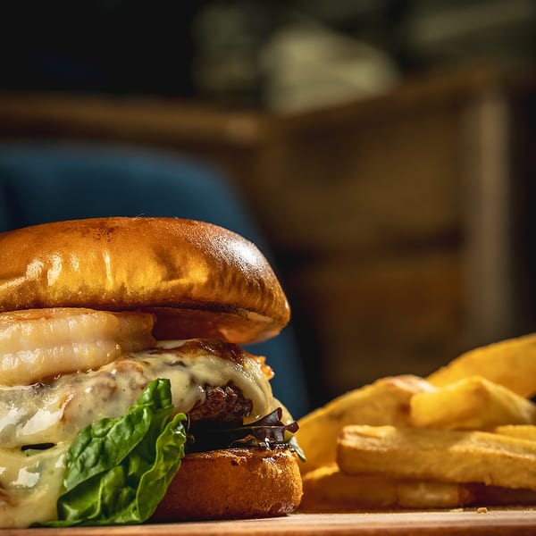 Gourmet burger with melted cheese, lettuce, and onion rings, served with fries on a wooden board.