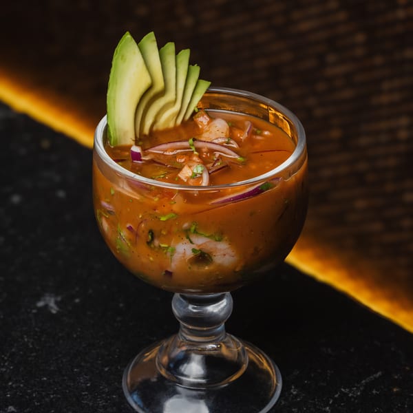 Shrimp ceviche in a glass goblet, garnished with avocado slices, red onion, and cilantro.
