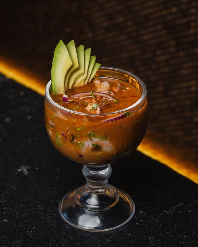 Shrimp ceviche in a glass, garnished with avocado slices, red onions, and cilantro.