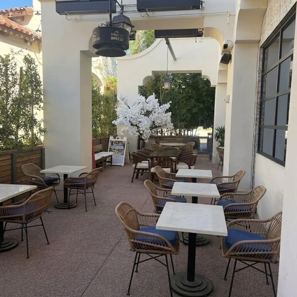 Outdoor patio with wicker chairs, white tables, and a decorative white cherry blossom tree.