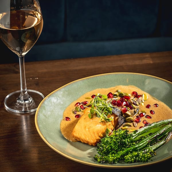 Salmon with mole sauce, pomegranate, pistachios, and broccolini, next to a glass of white wine.