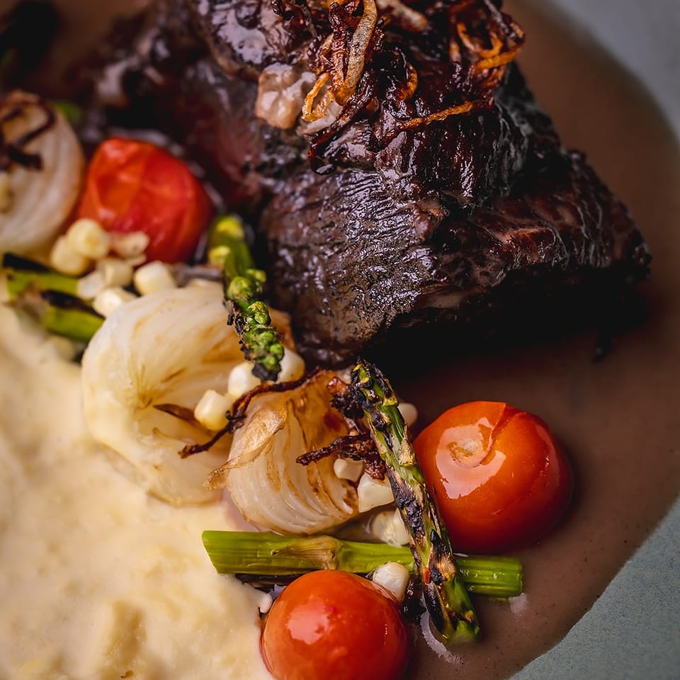 Glazed steak topped with crispy onions, served with mashed potatoes, roasted tomatoes, onions, corn, and asparagus.