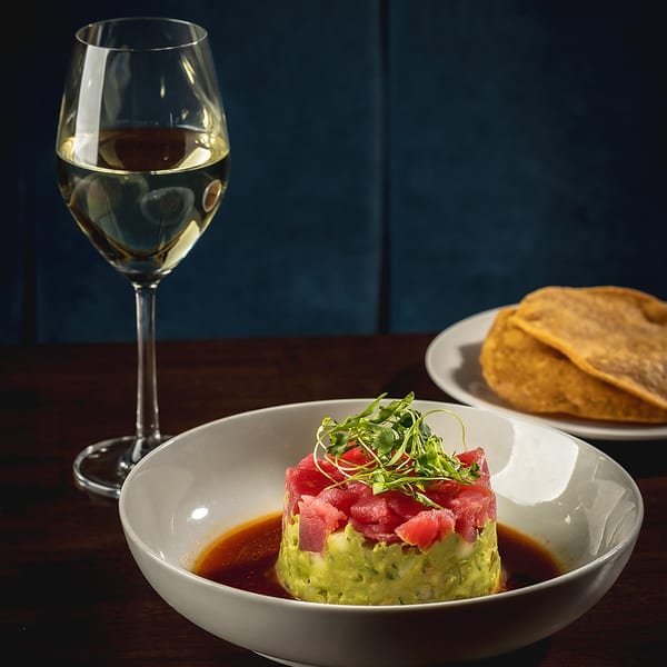 Tuna tartare with avocado, microgreens, and sauce, alongside a glass of white wine and tortillas.