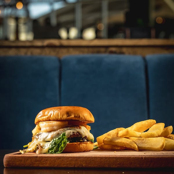 Gourmet burger with melted cheese and fries on a wooden board in a restaurant setting.