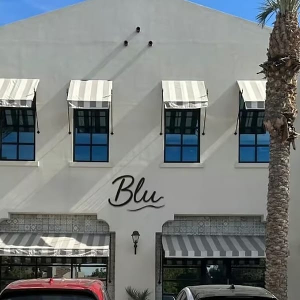 The white exterior of Blu restaurant with striped awnings, blue windows, and a palm tree.