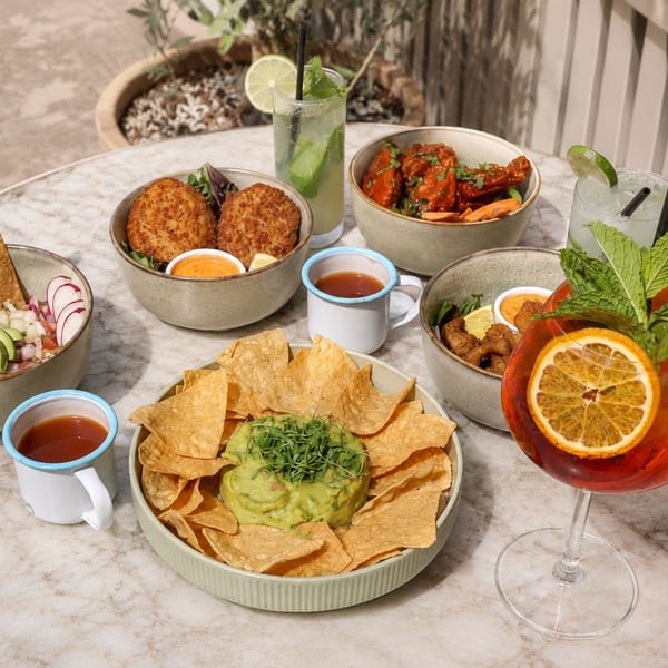 A marble table laden with various bowls of food, including guacamole, ceviche, and fried items, plus cocktails.