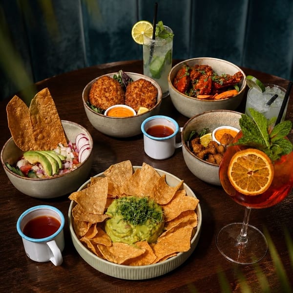 A wooden table laden with various dishes, including guacamole, ceviche, and cocktails.