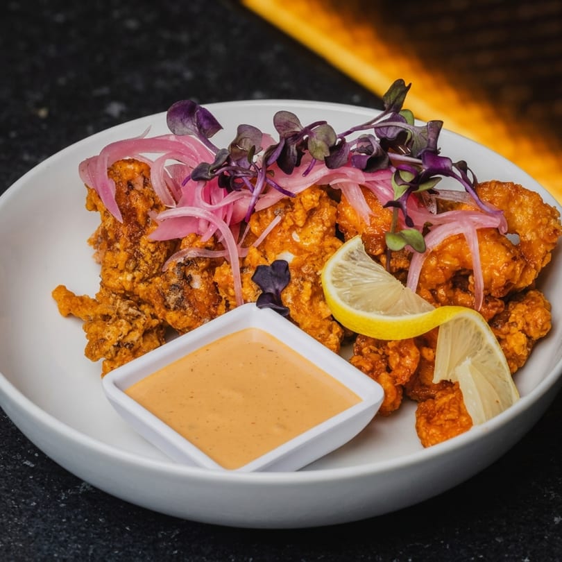 Crispy fried calamari with pickled red onions, microgreens, lemon wedges, and a side of sauce.