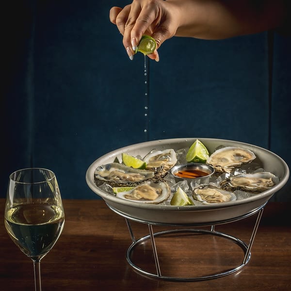 Hand squeezing lime over oysters on ice with a glass of white wine on a wooden table.