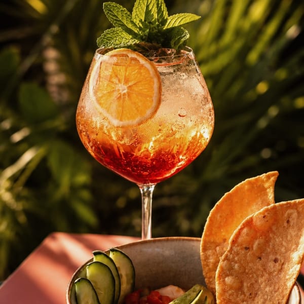 A vibrant orange cocktail with mint and citrus, next to a bowl of ceviche with tortilla chips.